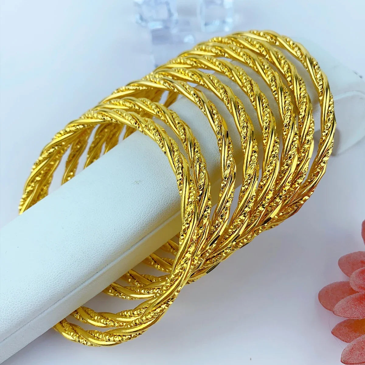 Stapel dünner, goldfarbener geometrischer Armreifen auf weißem Untergrund