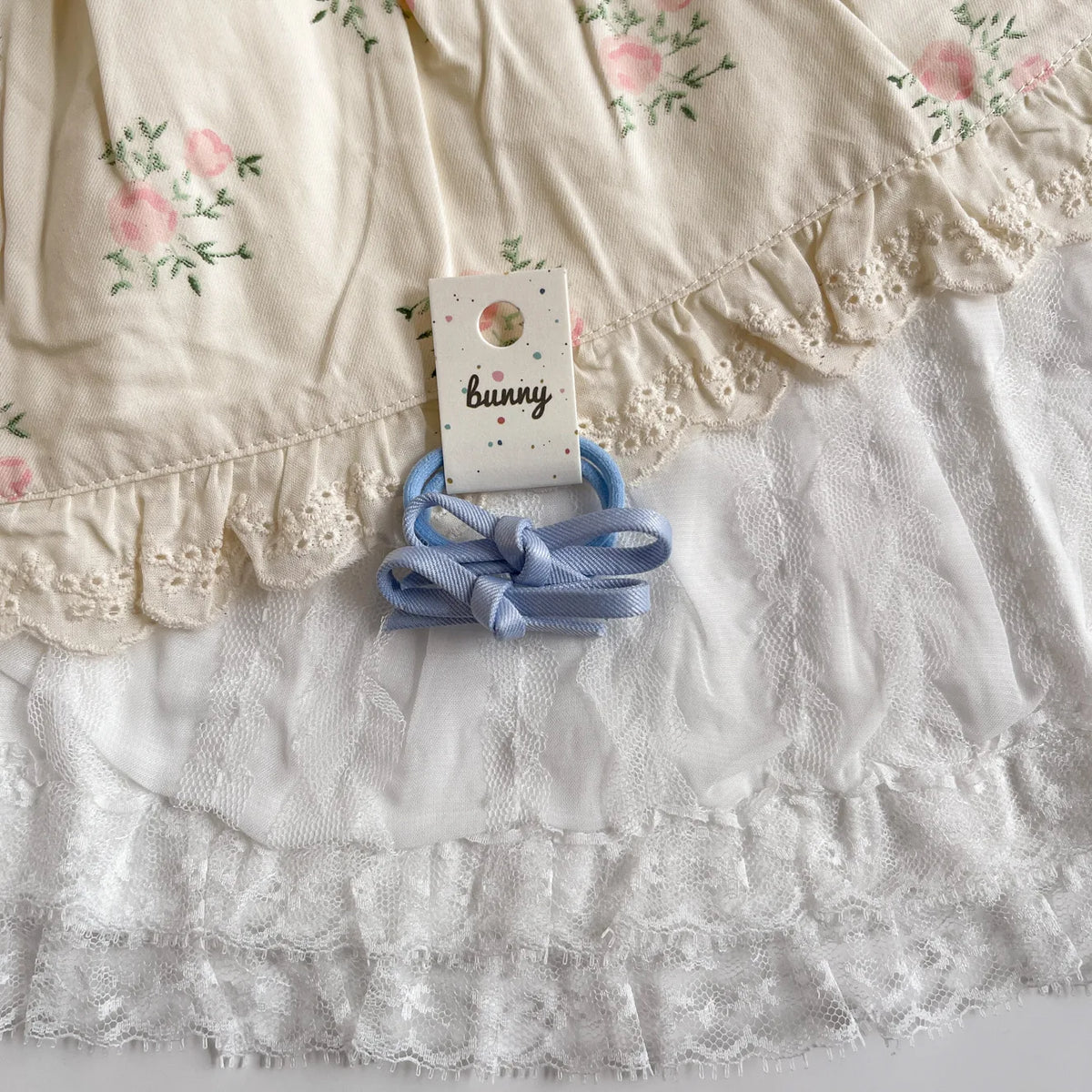 Un ensemble de pinces à cheveux en nœud papillon bleu clair avec une étiquette 'Bunny' sur tissu en dentelle blanche.