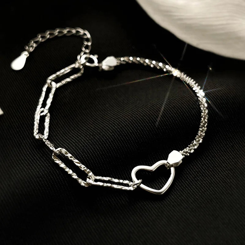A sterling silver double heart charm bracelet laid on a black surface.