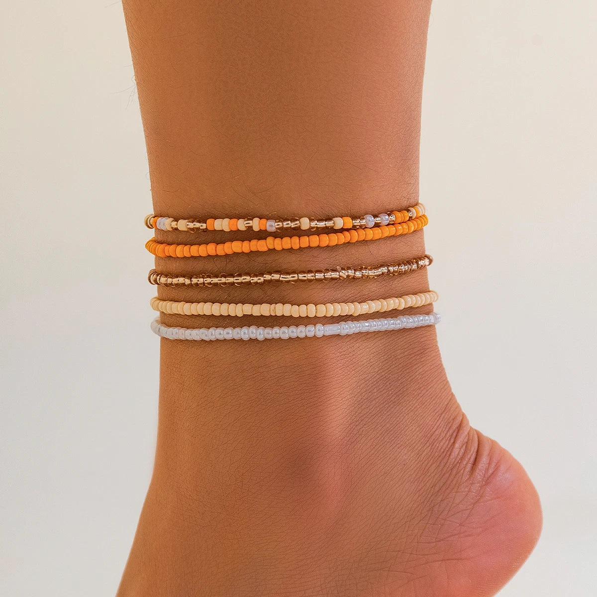 A stack of colorful seed bead anklets and bracelets worn on a person's ankle.