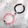 A pair of natural stone heart couple bracelets featuring black and pink beads on a white textured background.