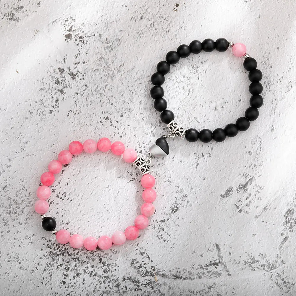 A pair of natural stone heart couple bracelets featuring black and pink beads on a white textured background.