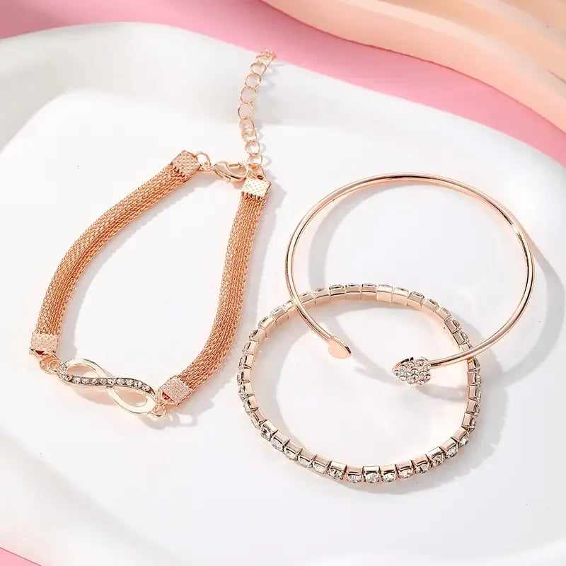 A set of three gold-toned heart charm bracelets with sparkling crystals displayed on a white surface.