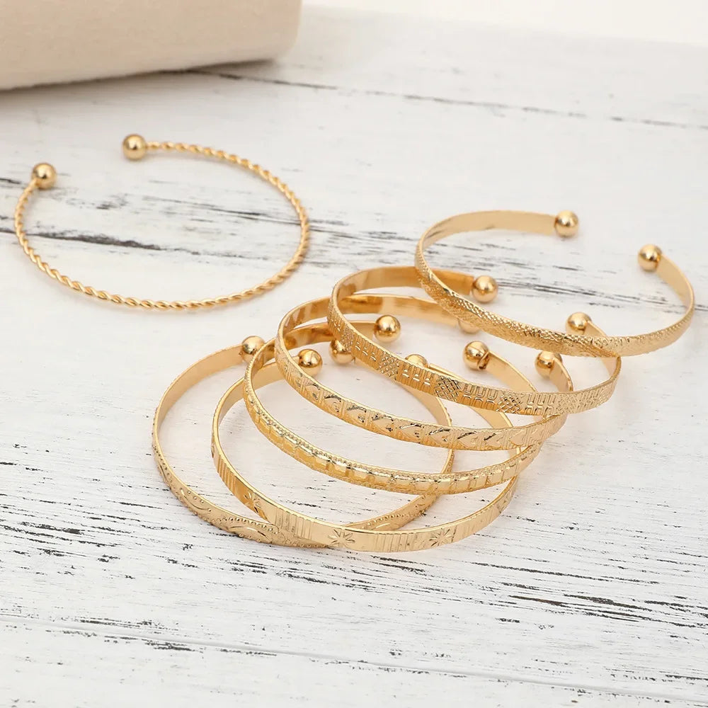 A set of elegant gold hexagon star twist bangles displayed on a white wooden surface.