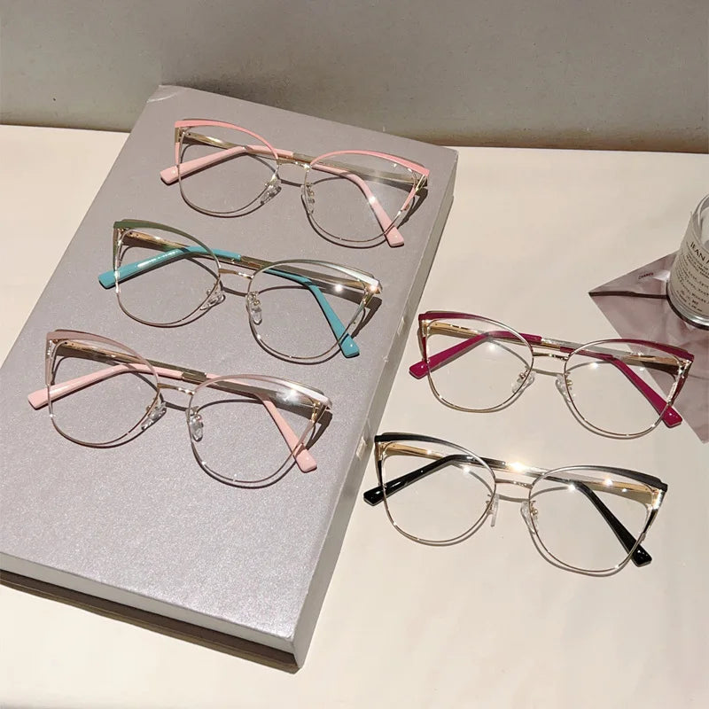 Colección de gafas de computadora estilo ojo de gato metálicas en rosa, azul y plata sobre una caja gris claro.