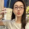 A woman wearing round anti-blue light computer glasses holds a disposable cup with a straw.