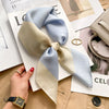A light blue and cream silk scarf tied in a bow, displayed on magazine pages.