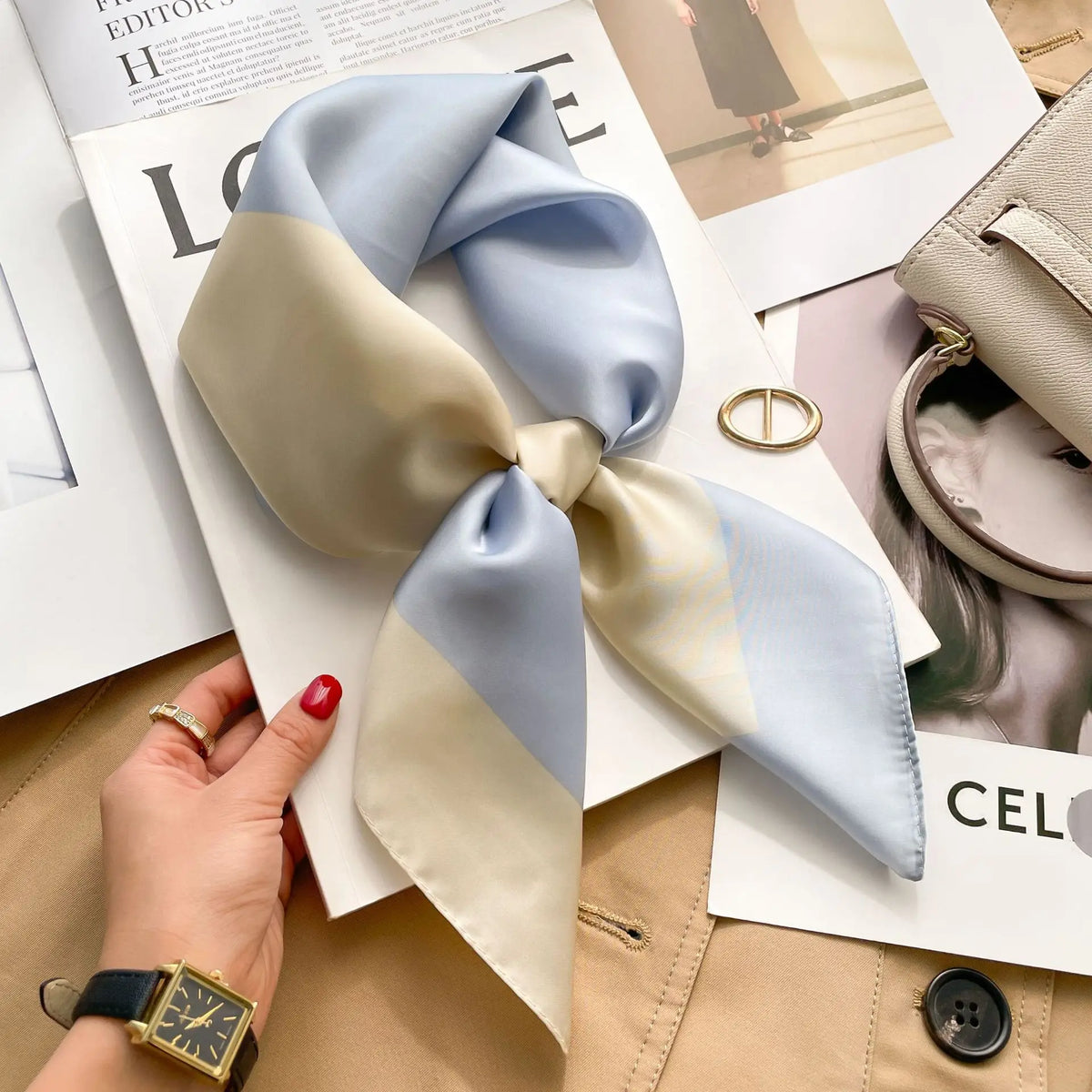 A light blue and cream silk scarf tied in a bow, displayed on magazine pages.