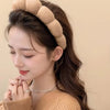 A woman wearing a beige cloud sponge hair accessory headband on her dark hair.