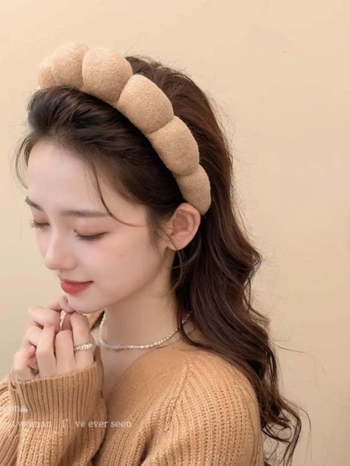 A woman wearing a beige cloud sponge hair accessory headband on her dark hair.
