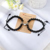 A pair of black natural stone heart couple bracelets resting on a light surface next to a piece of kraft paper.