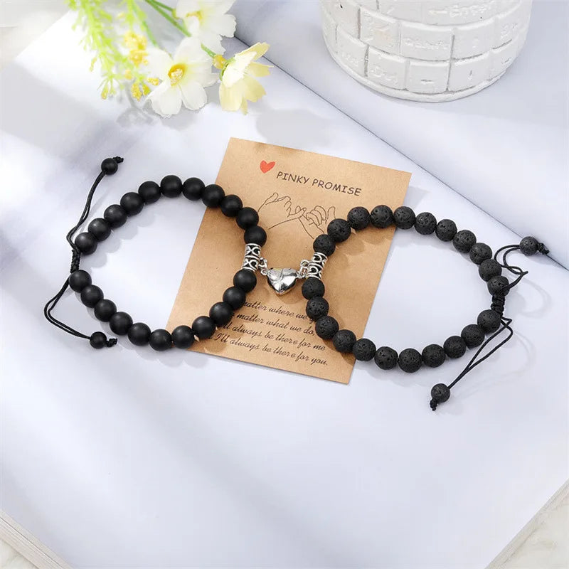 A pair of black natural stone heart couple bracelets resting on a light surface next to a piece of kraft paper.
