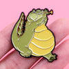 A cute green frog enamel pin with wings is shown being held by a hand.