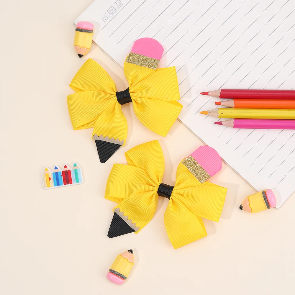 A set of cute pencil bow hair clips in yellow and pink, displayed on a white lined notepad.