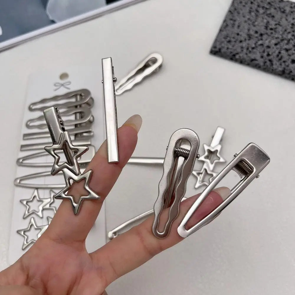 A hand holds a set of vintage silver Y2K metal hair clips and barrettes on a white surface.