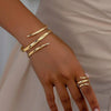 Une main portant un ensemble de bracelets et bagues géométriques dorés sur le poignet et les doigts.
