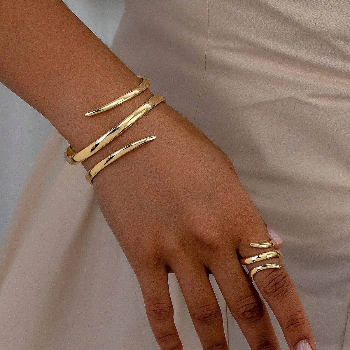 Une main portant un ensemble de bracelets et bagues géométriques dorés sur le poignet et les doigts.