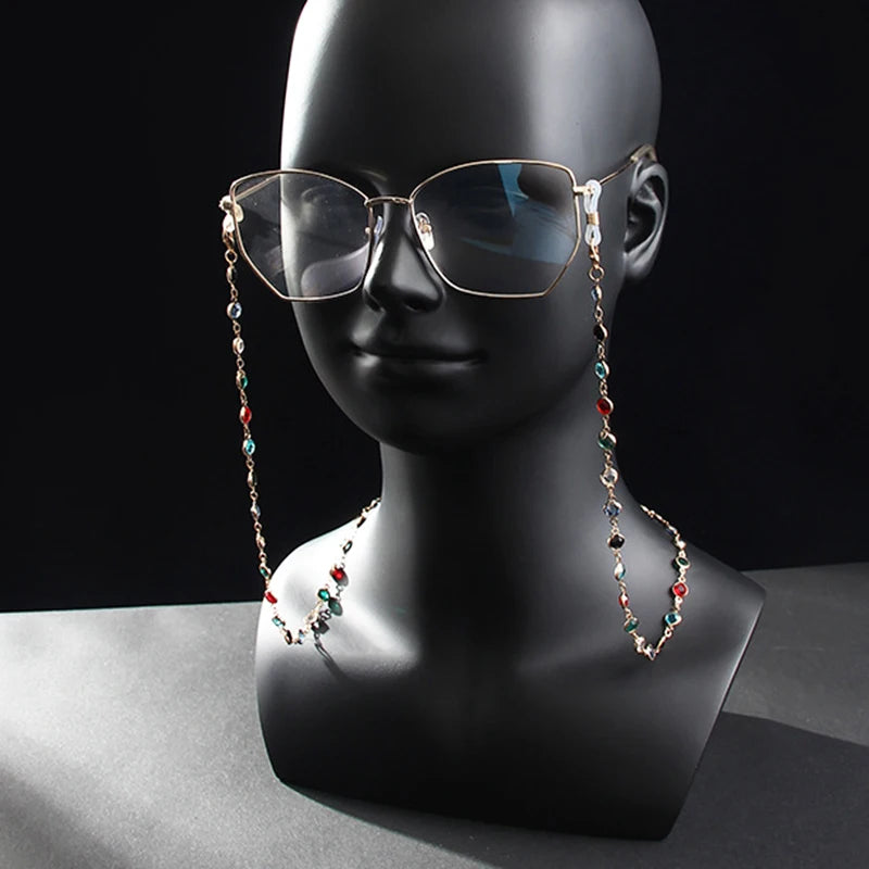 Un par de gafas de sol con marco dorado exhibidas en un maniquí con una delicada cadena de cuentas de cristal.