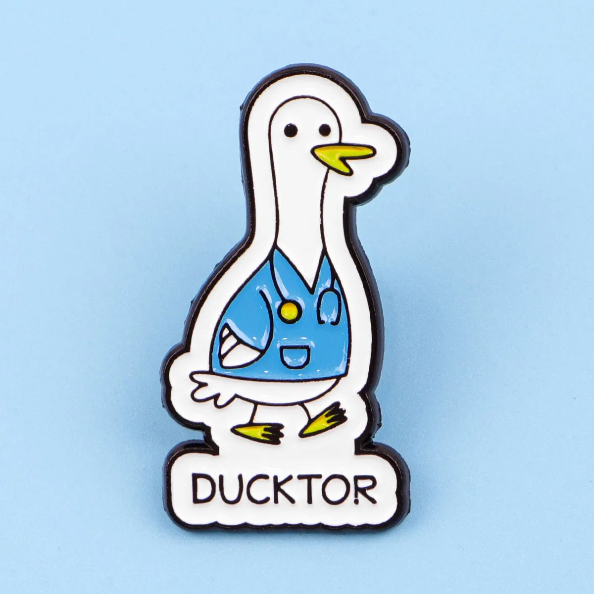 An enamel pin depicting a white duck doctor with a blue uniform and yellow accents.
