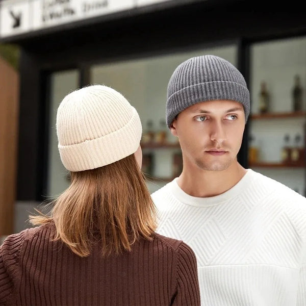 A man wearing a grey knitted beanie cap stands next to a woman with long brown hair, both in a modern indoor setting.