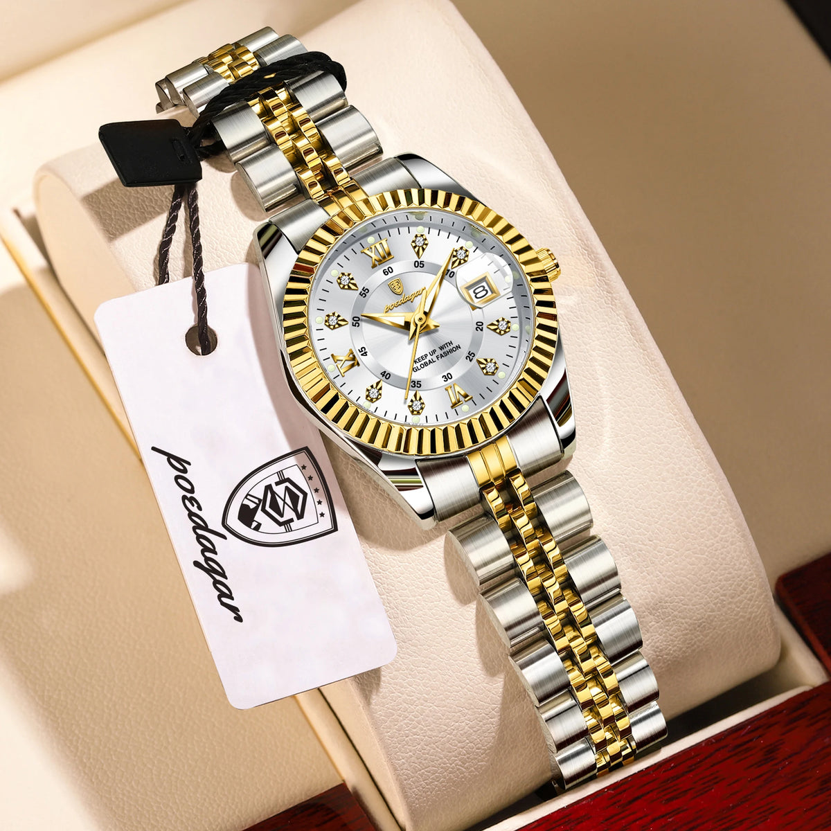 A silver and gold watch set with luminous hands and date display resting on a light-colored box.