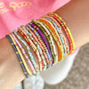 A stack of colorful beaded bangles worn on a wrist against a pink background.