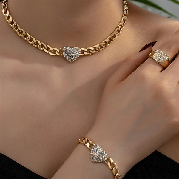 A close-up of a gold chain necklace with a heart charm and a matching gold bracelet on a woman's hand.