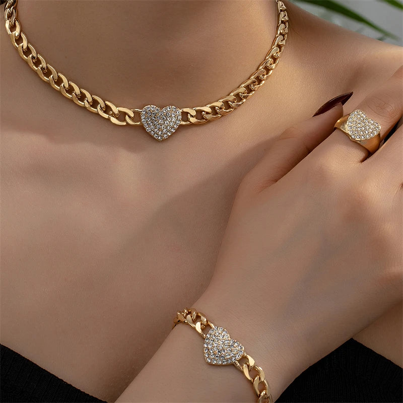 A close-up of a gold chain necklace with a heart charm and a matching gold bracelet on a woman's hand.
