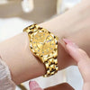 A close-up of a gold-toned mechanical watch with a sunburst dial and diamond accents worn on a wrist.