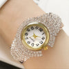 A close-up of an elegant quartz wristwatch covered in full rhinestones on a wrist.