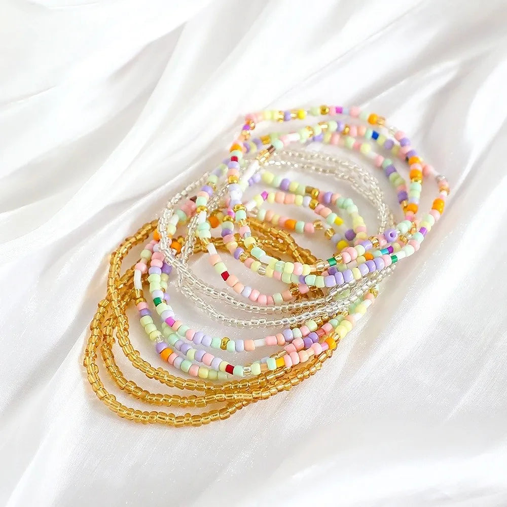 A stack of colorful beaded bangles in various shades of pink, yellow, and white laid on a white fabric.