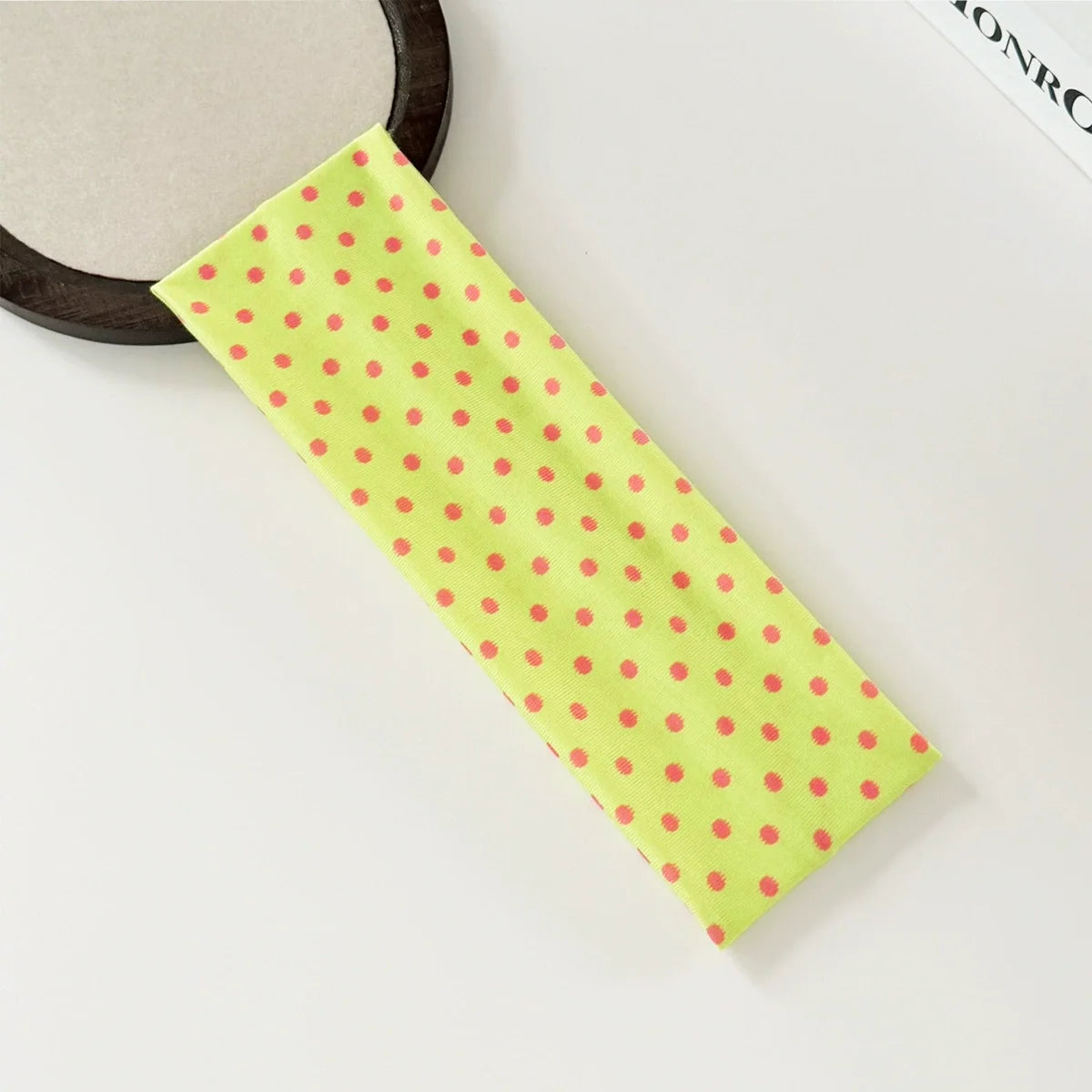 A bright lime green hairband with red polka dots is shown next to a wooden ring.