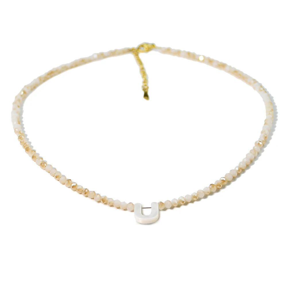 A delicate necklace featuring mother of pearl beads and crystal accents with a U-shaped initial charm.