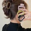 A hand is holding a set of square lightweight hair claw clips in various neutral tones, styled in a swept-back hairdo.