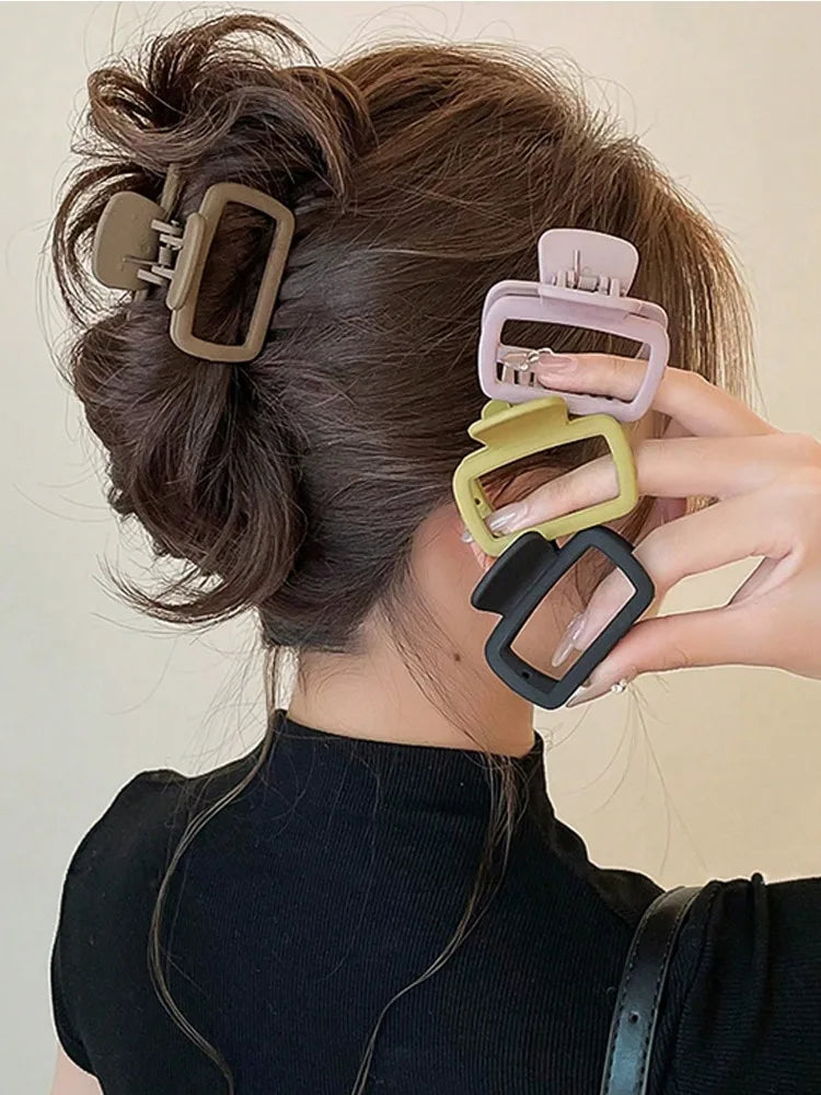 A hand is holding a set of square lightweight hair claw clips in various neutral tones, styled in a swept-back hairdo.