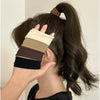 A hand is adjusting a stack of extra-wide elastic hair bands in various neutral tones against dark brown hair.