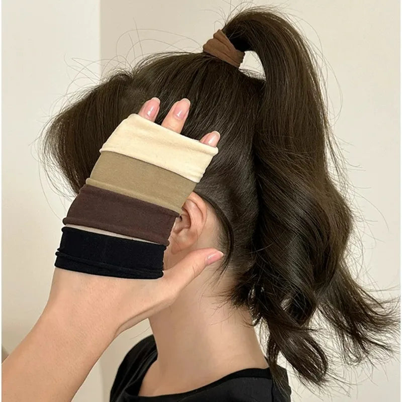 A hand is adjusting a stack of extra-wide elastic hair bands in various neutral tones against dark brown hair.