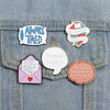 A set of five enamel pins featuring funny quotes on a denim fabric background.