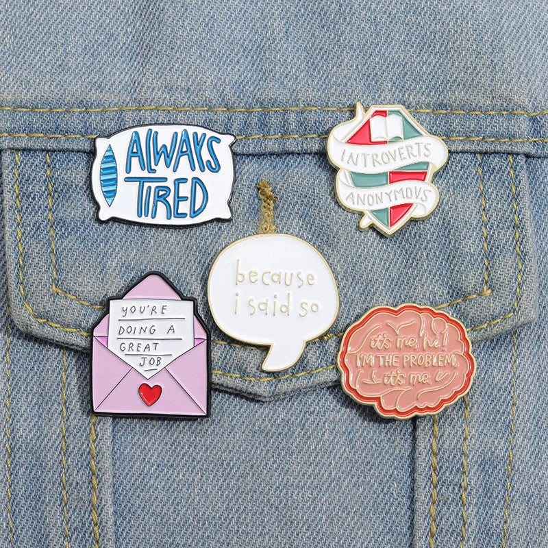A set of five enamel pins featuring funny quotes on a denim fabric background.