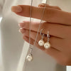 A hand models a dainty pearl jewelry set featuring matching earrings and a pendant necklace.
