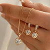A hand displays a delicate gold necklace with a heart pendant and matching small heart-shaped earrings.