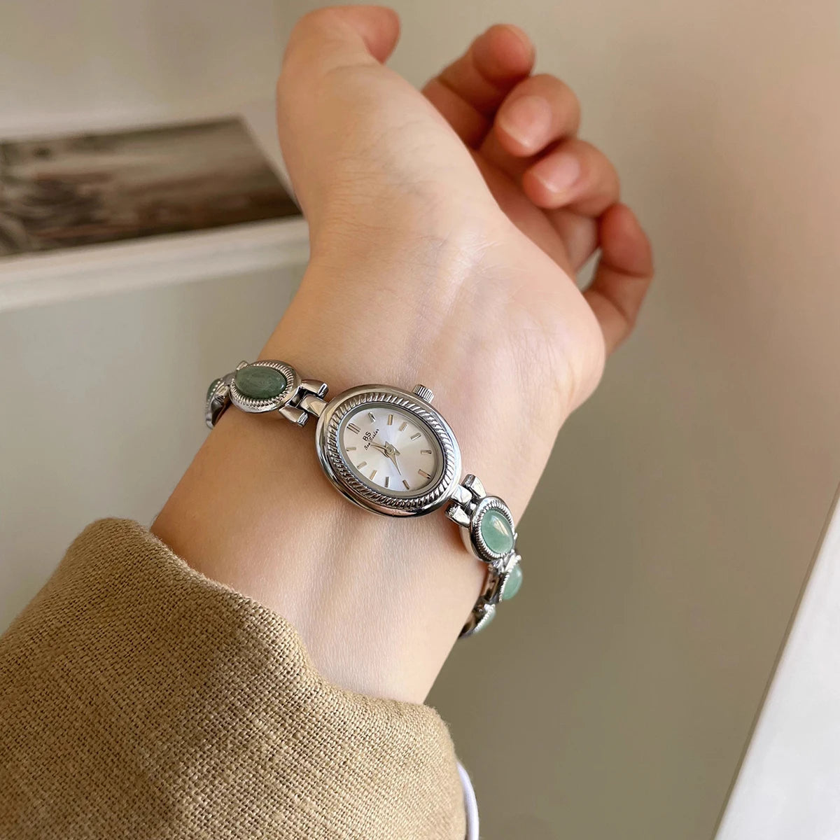 Gros plan sur le poignet d'une femme portant une élégante montre argentée avec des accents de quartz de jade vert.