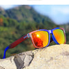 Blue and red gradient polarized sunglasses resting on a rocky surface with a blurred green mountain background.