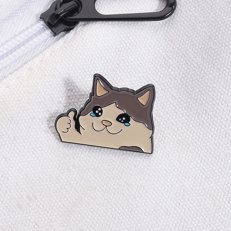 A cute enamel brooch pin of a cat with teary eyes and a smiling expression.