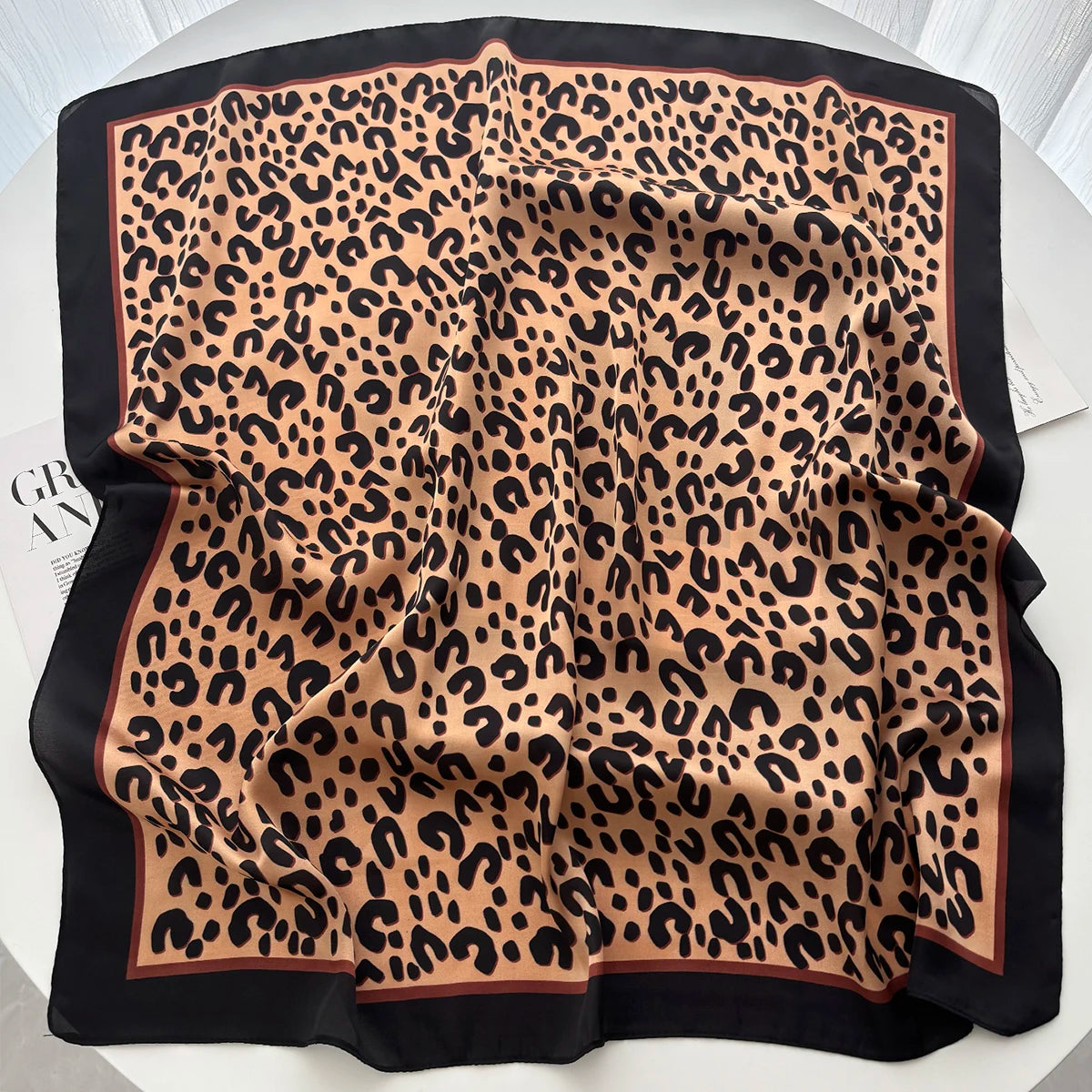 A black silk scarf featuring a leopard print in shades of brown and black.