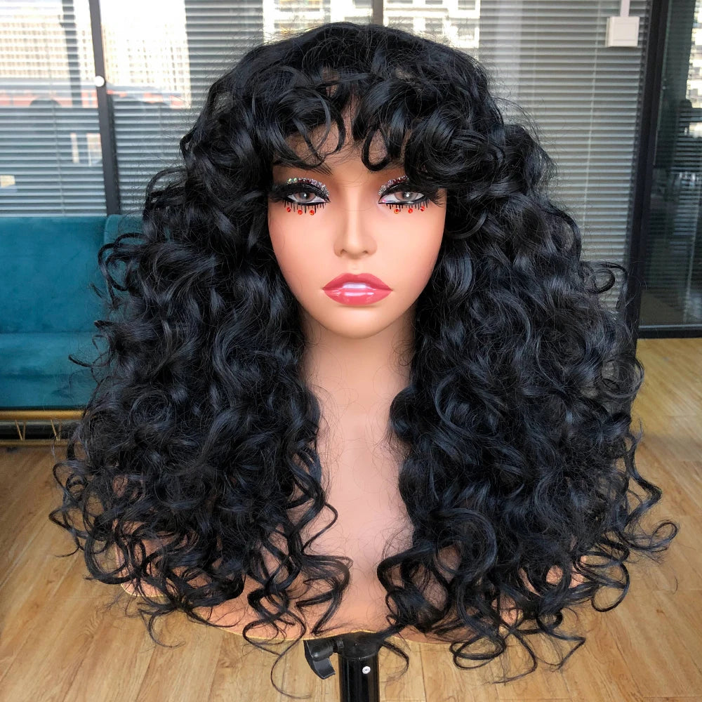 A model wears a long, black curly wave wig with bangs against a blurred background.