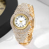 A close-up of an elegant gold quartz wristwatch fully encrusted with clear rhinestones on a white background.
