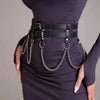 Un vestido morado oscuro usado con un cinturón de arnés de cuero falso negro con cadenas y hebillas plateadas.