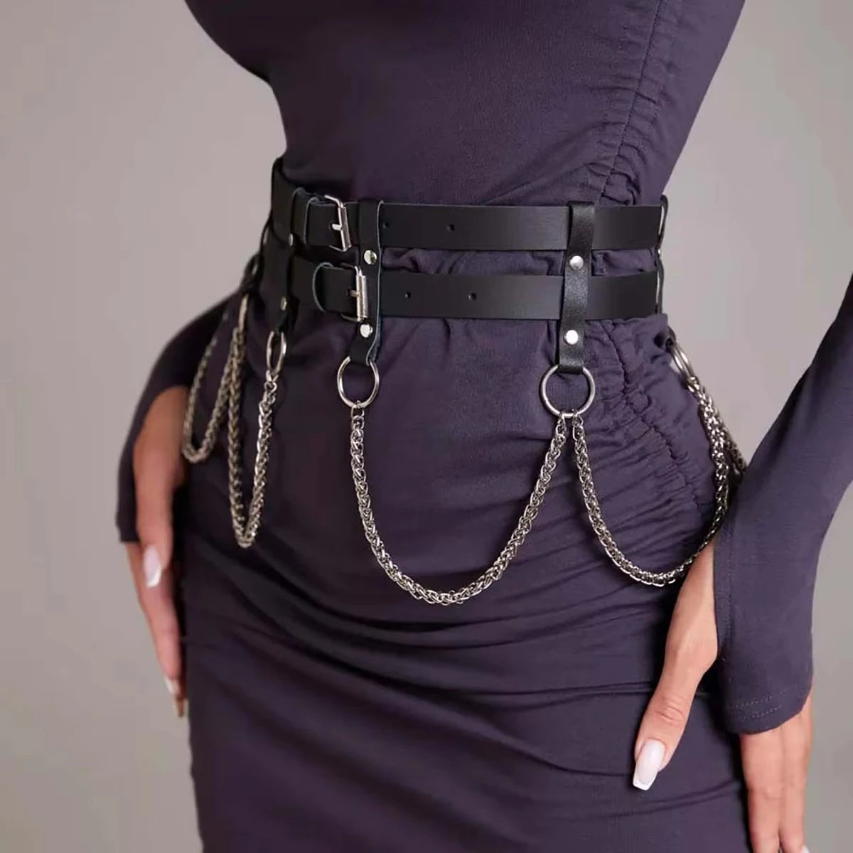 Un vestido morado oscuro usado con un cinturón de arnés de cuero falso negro con cadenas y hebillas plateadas.