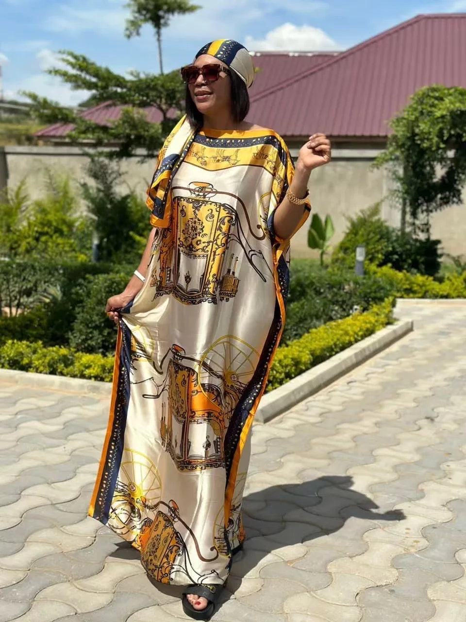 Eine Frau trägt ein fließendes, bedrucktes Kaftankleid in Beige- und Goldtönen im Freien.